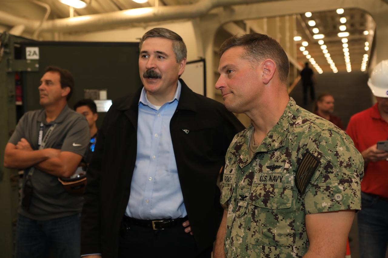 Captain Anthony Roach, at right, commanding officer in the U.S. Navy, speaks with NASA's Exploration Mission-1 (EM-1) Mission Manager Mike Sarafin during a familiarization tour with the Exploration Ground Systems (EGS) recovery team on Oct. 29, 2018, as they prepare for Underway Recovery Test-7 (URT-7) onboard a U.S. Navy ship. The team is responsible for recovering the Orion crew capsule after it flies farther than any human-rated spacecraft has flown, with EM-1. EGS and the U.S. Navy will use a test version of the Orion crew module, several rigid hull inflatable boats and support equipment to verify and validate processes, procedures, hardware and personnel during recovery of Orion in open waters. URTs are a series of tests to ensure all systems are go when recovering the Orion crew capsule and astronauts onboard in the future. Orion will have emergency abort capability, sustain the crew during space travel and provide safe re-entry from deep space return velocities.