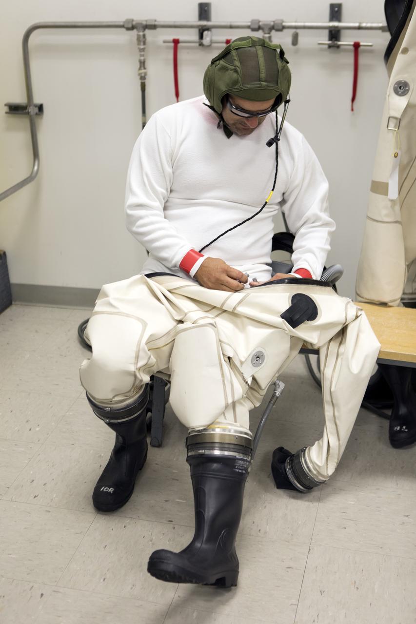 An operator dons a Self-Contained Atmospheric Protective Ensemble (SCAPE) suit inside a room in the Multi-Payload Processing Facility (MPPF) at NASA's Kennedy Space Center in Florida on Oct. 31, 2018. SCAPE operators, wearing the suits, will participate in a hypergolic systems hot flow test at the MPPF. The test will serve as operational validation of the hypergol subsystem and demonstrate that the hypergols subsystem can service the Orion spacecraft, flow fuel at the required rates, drain and de-service the system, and meet the intended timeline. SCAPE suite are used in operations involving toxic propellants and are supplied with air either through a hardline or through a self-contained environmental control unit.