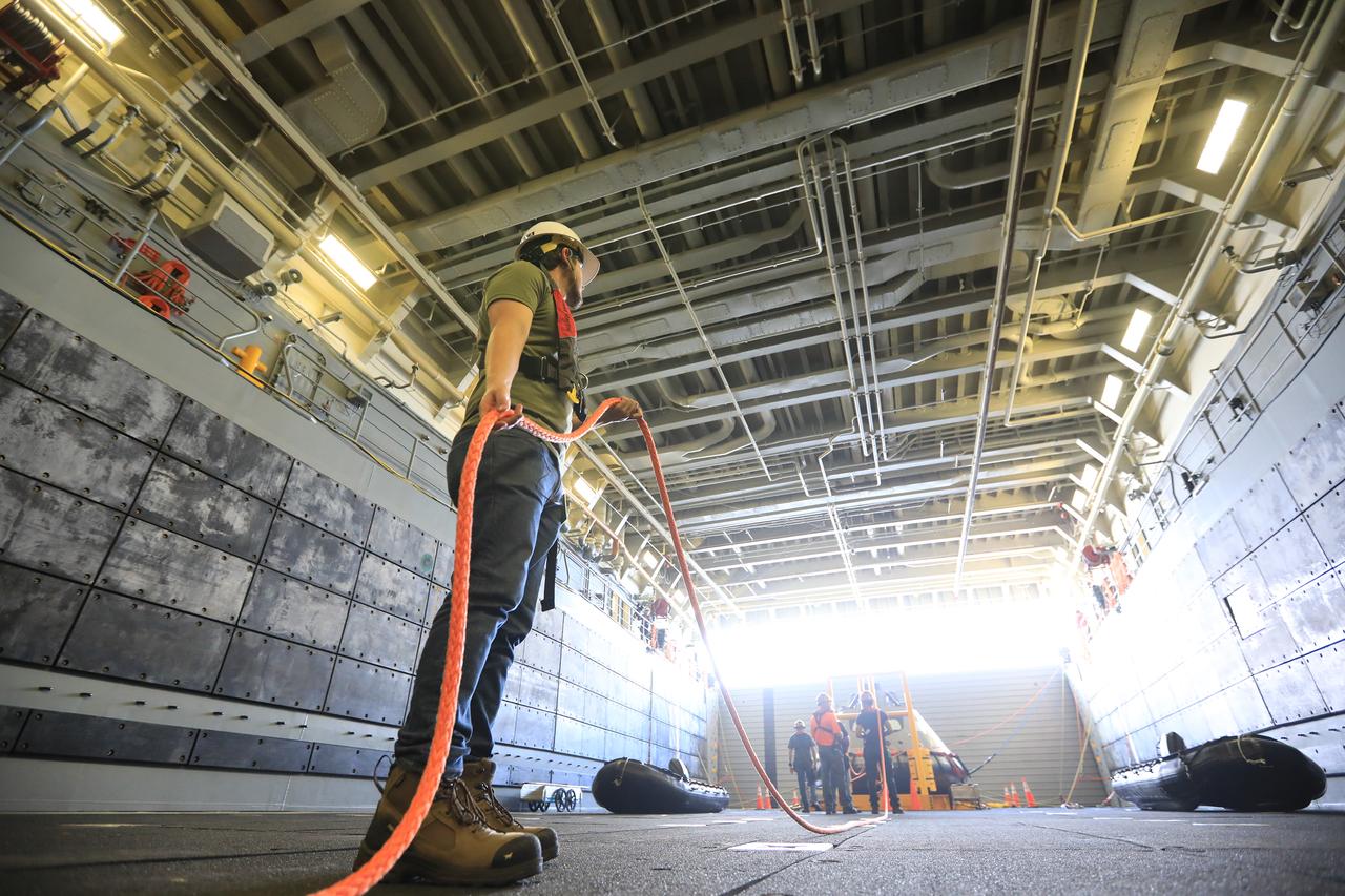 Jose Martinez, an instrumentation engineer with Jacobs, runs the winch line out to the test version of the Orion capsule in the well deck of the USS John P. Murtha, during Underway Recovery Test-7 (URT-7) on Oct. 31, 2018, in the Pacific Ocean. Exploration Ground Systems and the U.S. Navy are using the mock Orion to verify and validate processes, procedures, hardware and personnel during recovery of Orion in open waters. URTs are a series of tests to verify and validate procedures and hardware that will be used to recover the Orion spacecraft after it splashed down in the Pacific Ocean following deep space exploration missions. Orion will have emergency abort capability, sustain the crew during space travel and provide safe re-entry from deep space return velocities.