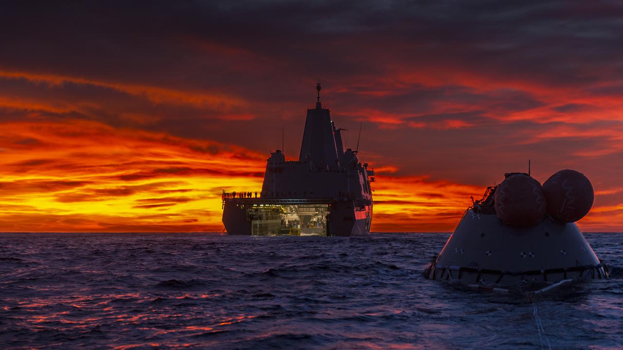 The USS John P. Murtha and a test version of the Orion capsule are in view at sunset on Nov. 1, 2018, during Underway Recovery Test-7 (URT-7) in the Pacific Ocean. URT-7 is one in a series of tests that the Exploration Ground Systems Recovery Team, along with the U.S. Navy, are conducting to verify and validate procedures and hardware that will be used to recover the Orion spacecraft after it splashes down in the Pacific Ocean following deep space exploration missions. Orion will have emergency abort capability, sustain the crew during space travel and provide safe re-entry from deep space return velocities.