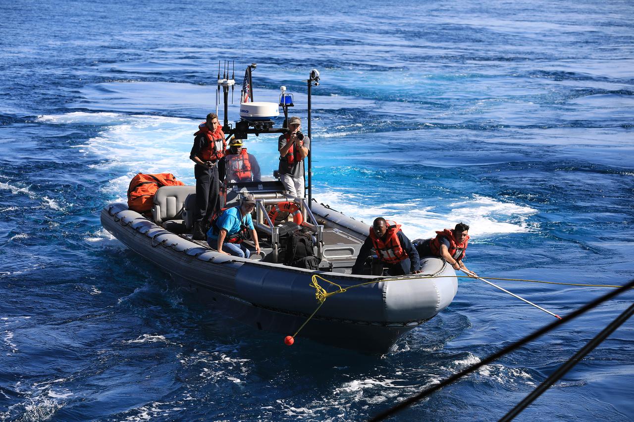 From the USS John P. Murtha, Engineman 2nd Class Christian Maldonado, at right, reaches for a tending line that Seaman Dante Jones, at left, will grab. The crew will then attach the line to the test version of the Orion capsule to help guide into the ship's well deck during Underway Recovery Test-7 (URT-7) on Nov. 1, 2018. URT-7 is one in a series of tests to verify and validate procedures and hardware that will be used to recover the Orion spacecraft after it splashes down in the Pacific Ocean following deep space exploration missions. Orion will have emergency abort capability, sustain the crew during space travel and provide safe re-entry from deep space return velocities.