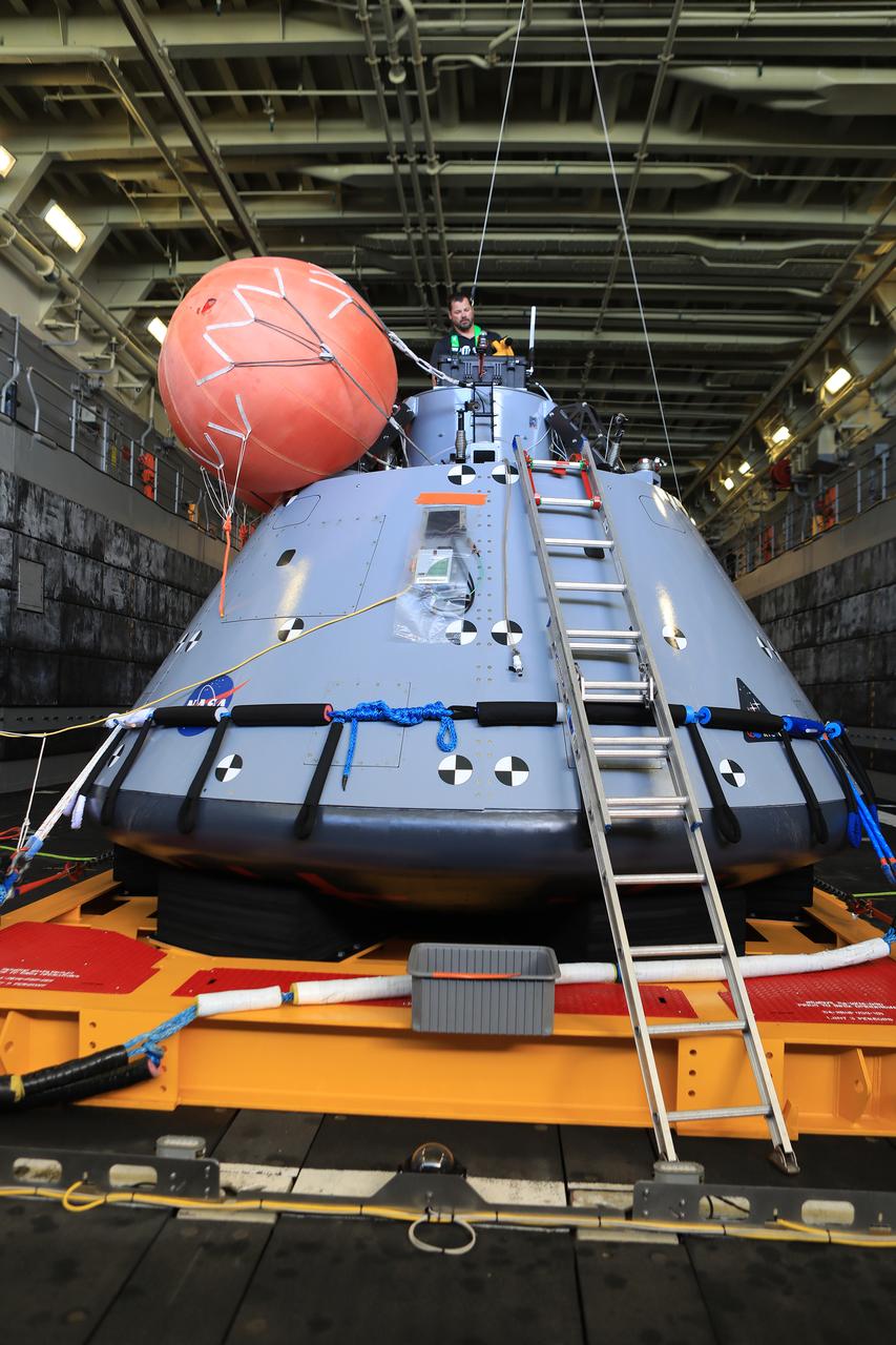 Open Water Recovery Lead Tim Goddard attaches lights to the top of the test version of the Orion capsule used during Underway Recovery Test-7 (URT-7) in the well deck of the USS John P. Murtha on Nov. 3, 2018. Goddard is the hardware expert in the open water and assists dive teams in the Pacific Ocean as they practice recovering the capsule during day and nighttime conditions. URT-7 is one in a series conducted by the Exploration Ground Systems Recovery Team to verify and validate procedures and hardware that will be used to recover the Orion spacecraft after it splashes down in the Pacific Ocean following deep space exploration missions. Orion will have emergency abort capability, sustain the crew during space travel and provide safe re-entry from deep space return velocities.