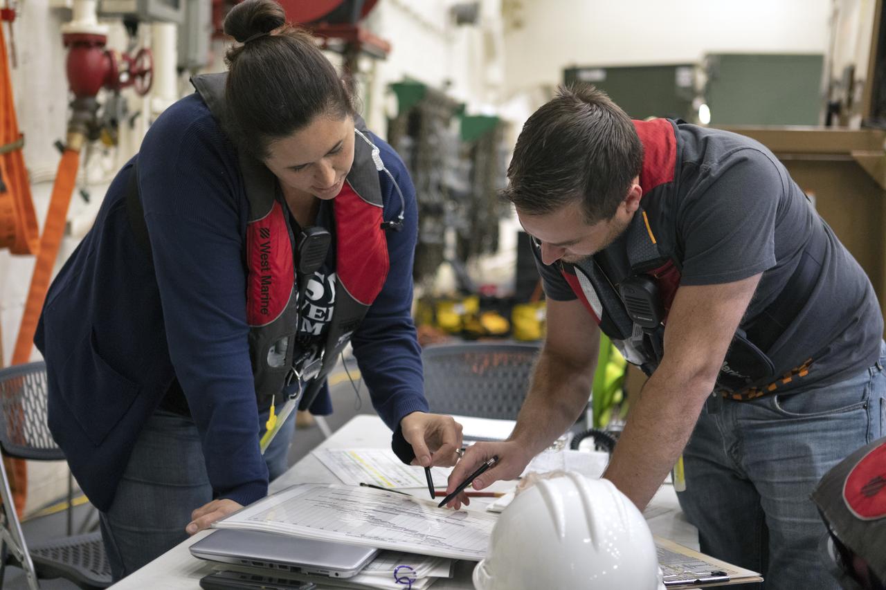 NASA Landing and Recovery Director Melissa Jones, left, reviews procedures with a recovery team member inside the USS John P. Murtha on Nov. 4, 2018, during Underway Recovery Test-7. During URT-7, the team practices recovering a test version of the Orion capsule from the Pacific Ocean and towing it into the well deck of the ship. URT-7 is one in a series of tests conducted by the Exploration Ground Systems Recovery Team to verify and validate procedures and hardware that will be used to recover the Orion spacecraft after it splashes down in the Pacific Ocean following deep space exploration missions. Orion will have emergency abort capability, sustain the crew during space travel and provide safe re-entry from deep space return velocities.