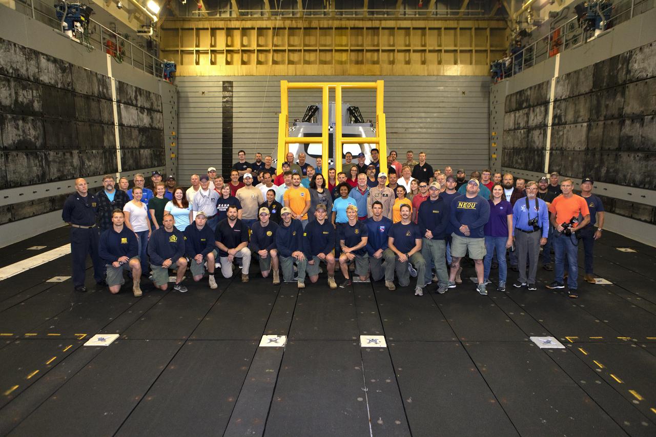 NASA's Recovery Team takes time for a group photo in the well deck of the USS John P. Murtha, during Underway Recovery Test-7 (URT-7) on Nov. 5, 2018. Behind them is the test version of the Orion capsule. The Recovery Team, along with the U.S. Navy, practice recovering the Orion test version as part of URT-7 in the Pacific Ocean. URT-7 is one in a series of tests to verify and validate procedures and hardware that will be used to recover the Orion spacecraft after it splashes down in the Pacific Ocean following deep space exploration missions. Orion will have emergency abort capability, sustain the crew during space travel and provide safe re-entry from deep space return velocities.
