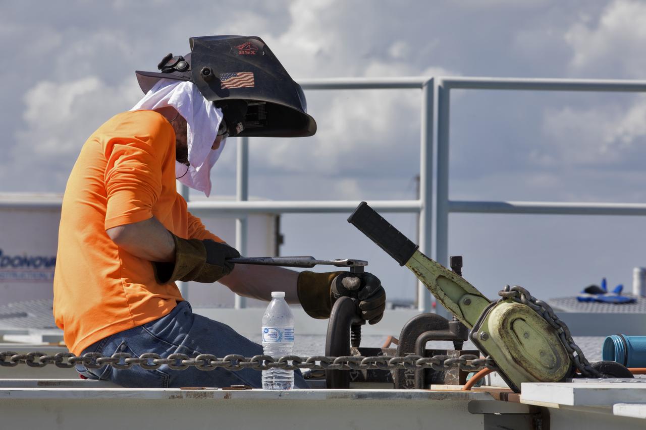 To continue his work, a construction worker secures clamps on a section of metal on the surface of Launch Pad 39B at NASA's Kennedy Space Center in Florida on July 26, 2018. The launch pad has undergone upgrades and modifications to accommodate NASA's Space Launch System and Orion spacecraft for Exploration Mission-1 and subsequent missions. Upgrades include new heat-resistant bricks on the walls of the flame trench and installation of a new flame deflector. All of the upgrades have been managed by Exploration Ground Systems.