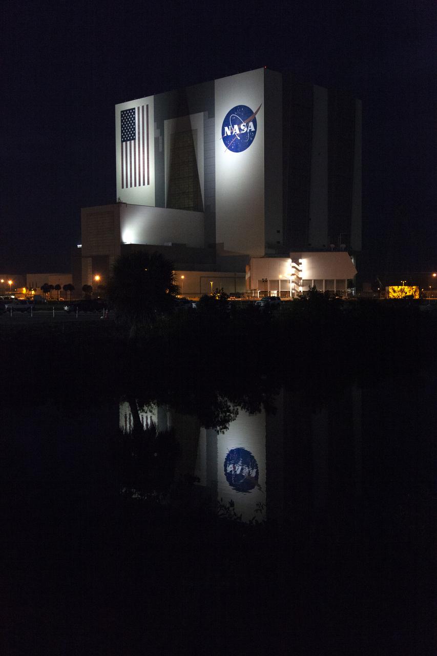 The iconic Vehicle Assembly Building (VAB) and Launch Control Center cast reflections on the surface of a nearby waterway at NASA’s Kennedy Space Center in Florida. The lights illuminating the VAB provided a splendid nighttime view. 