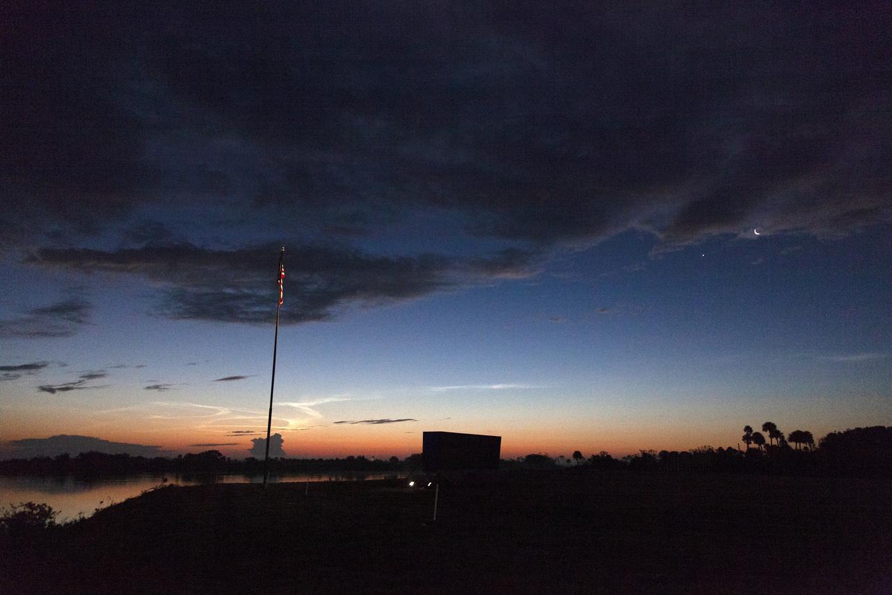 A sunrise serves as the backdrop for the countdown clock and American Flag near the Press Site at NASA’s Kennedy Space Center in Florida following the successful launch of SpaceX’s uncrewed Demo-1 flight test from Launch Complex 39A on March 2, 2019. The company’s Crew Dragon spacecraft lifted off atop a Falcon 9 rocket and traveled to the International Space Station, where it validated end-to-end systems and capabilities in preparation for certification to fly crew. 
