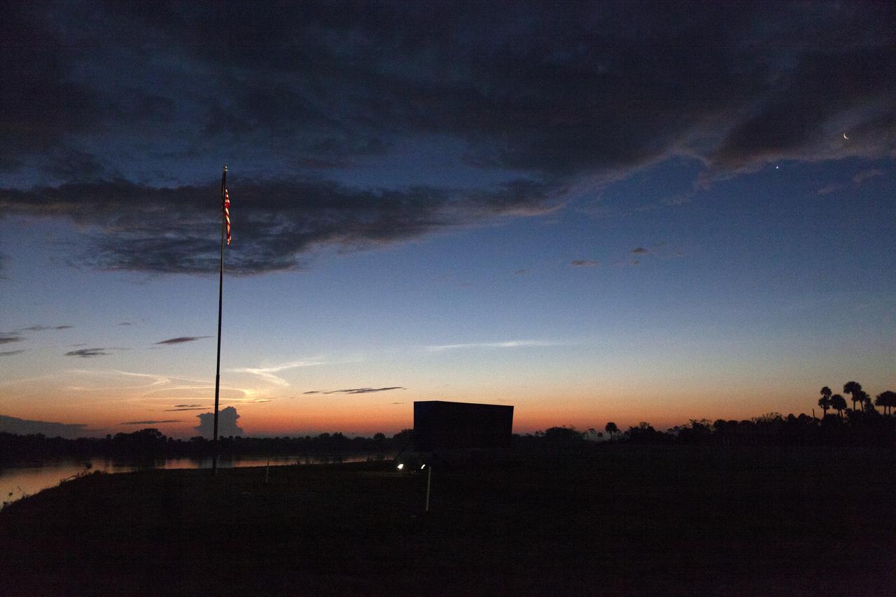 A sunrise serves as the backdrop for the countdown clock and American Flag near the Press Site at NASA’s Kennedy Space Center in Florida following the successful launch of SpaceX’s uncrewed Demo-1 flight test from Launch Complex 39A on March 2, 2019. The company’s Crew Dragon spacecraft lifted off atop a Falcon 9 rocket and traveled to the International Space Station, where it validated end-to-end systems and capabilities in preparation for certification to fly crew. 