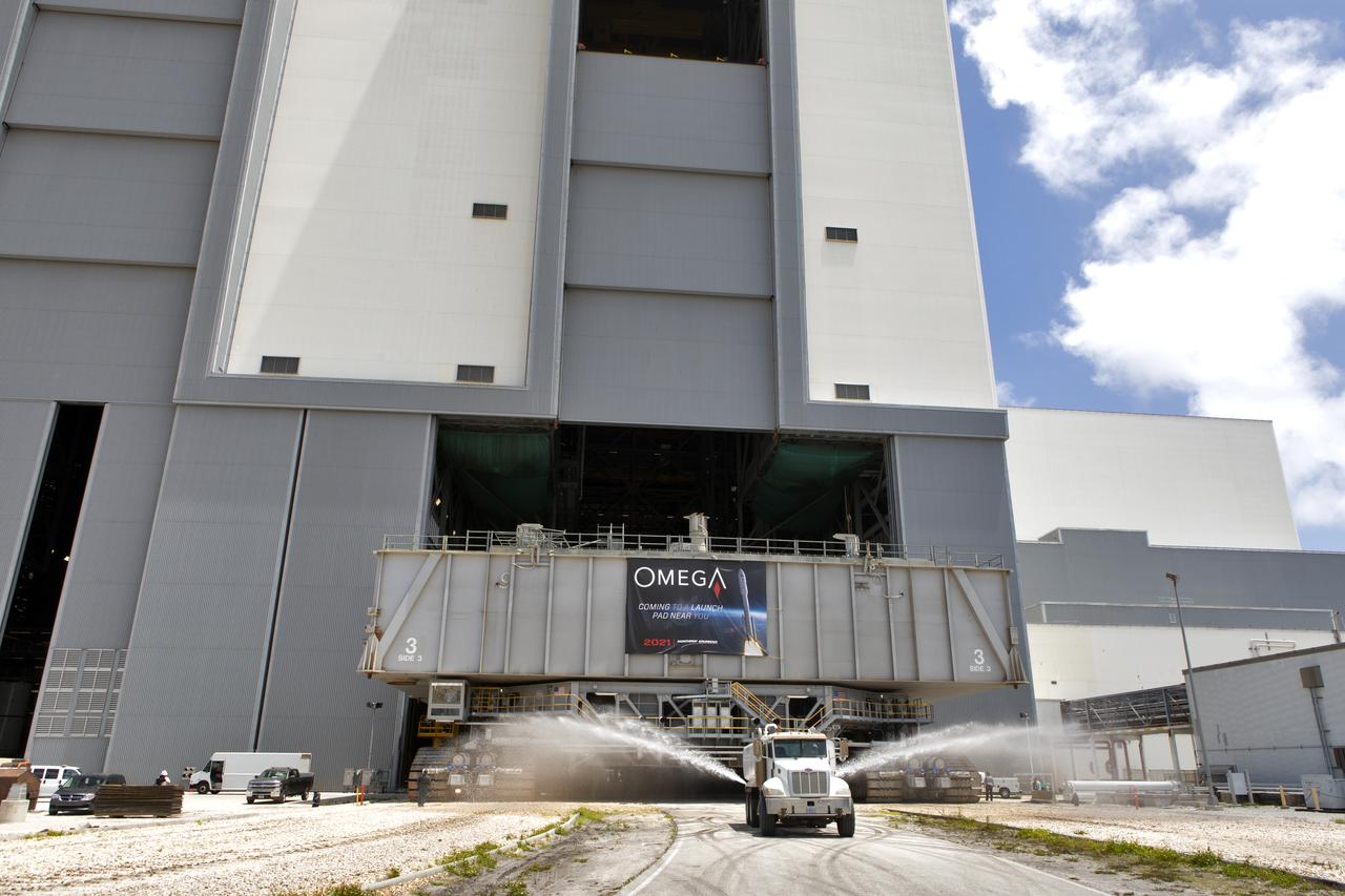 During a practice run, crawler-transporter 2 (CT-2), with the space shuttle-era mobile launch platform-3 (MLP-3) on top, moves out of High Bay 2 of the Vehicle Assembly Building (VAB) at NASA’s Kennedy Space Center in Florida on May 1, 2019. A truck in front sprays water to reduce dust on the crawlerway. The VAB is getting its first commercial tenant. Northrop Grumman signed a Reimbursable Space Act Agreement with NASA for use of the facilities. The company will assemble and test its new OmegA rocket inside the massive facility’s High Bay 2. The company also will modify MLP-3 to serve as the launch vehicle’s assembly and launch platform. Northrop Grumman is developing the OmegA rocket, an intermediate/heavy-class launch vehicle, as part of a launch services agreement with the U.S. Air Force.