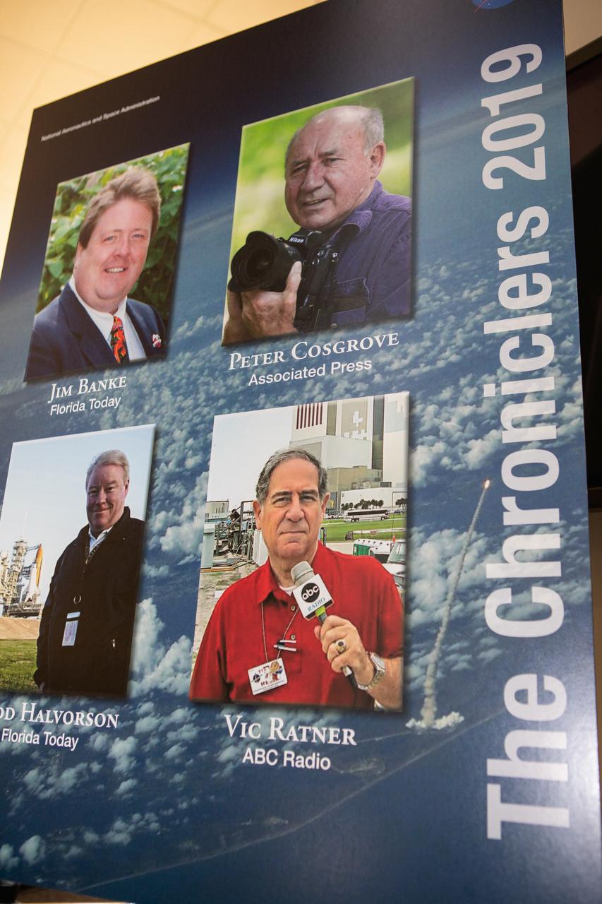 A poster bearing the names and photos of the four new honorees distinguished as Chroniclers stands in Kennedy Space Center’s NASA News Center in Florida during a ceremony on May 3, 2019. The Chroniclers recognizes retirees of the news and communications business who have helped spread news of American space exploration from Kennedy for 10 years or more. From top left to bottom right are Jim Banke, Florida Today; Peter Cosgrove, Associated Press photographer; Todd Halvorson, Florida Today; and Vic Ratner, ABC Radio. The group of four was selected by a committee of their peers on March 25. 