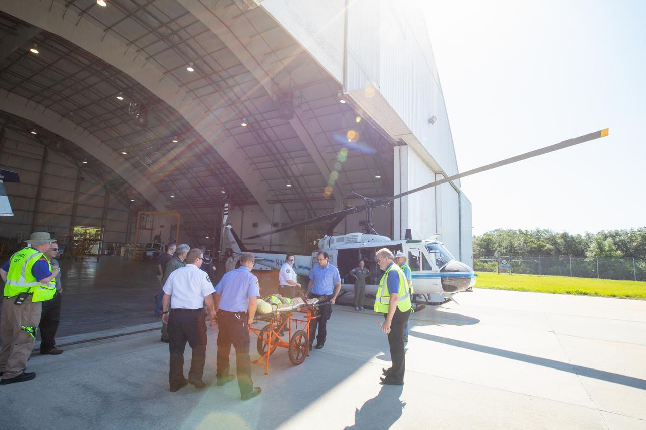 Kennedy Space Center personnel and American Medical Response (AMR) contractor paramedics gather around a “patient,” a KEMCON Fitness Center staff member, during a medical support training course in the Space Florida hangar at the spaceport’s Shuttle Landing Facility on May 17, 2019. The course was designed to familiarize the AMR paramedics with the center’s Triage Forces deployment, which included medical team members, fire/rescue personnel, environmental health specialists and flight operations crew members, as well as a helicopter, Mine Resistant Ambush Protected (MRAP) tactical vehicle, fire pumper truck and triage vehicles. The AMR paramedics will assist the agency in contingency planning for the return of human spaceflight from Kennedy.
