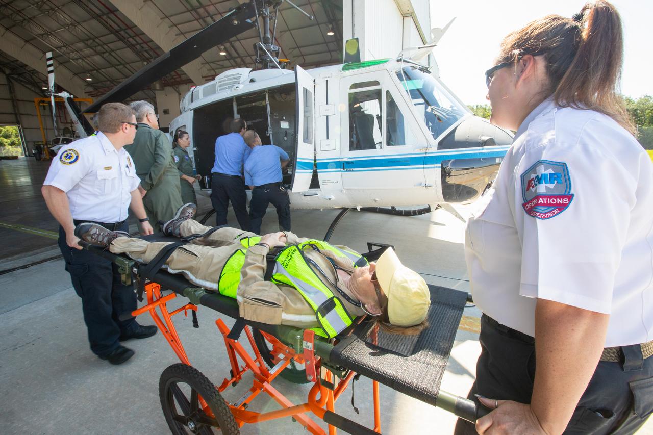 Kennedy Space Center personnel and American Medical Response (AMR) contractor paramedics prepare to load a “patient,” a KEMCON Fitness Center staff member, into a NASA helicopter during a medical support training course in the Space Florida hangar at the spaceport’s Shuttle Landing Facility on May 17, 2019. The course was designed to familiarize the AMR paramedics with the center’s Triage Forces deployment, which included medical team members, fire/rescue personnel, environmental health specialists and flight operations crew members, as well as a helicopter, Mine Resistant Ambush Protected (MRAP) tactical vehicle, fire pumper truck and triage vehicles. The AMR paramedics will assist the agency in contingency planning for the return of human spaceflight from Kennedy.