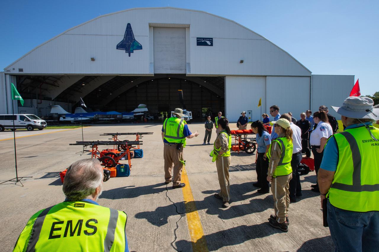 Kennedy Space Center personnel and American Medical Response (AMR) contractor paramedics gather near the Space Florida hangar at the spaceport’s Shuttle Landing Facility on May 17, 2019, for a medical support training course. The course was designed to familiarize the AMR paramedics with the center’s Triage Forces deployment, which included medical team members, fire/rescue personnel, environmental health specialists and flight operations crew members, as well as a helicopter, Mine Resistant Ambush Protected (MRAP) tactical vehicle, fire pumper truck and triage vehicles. The AMR paramedics will assist the agency in contingency planning for the return of human spaceflight from Kennedy.