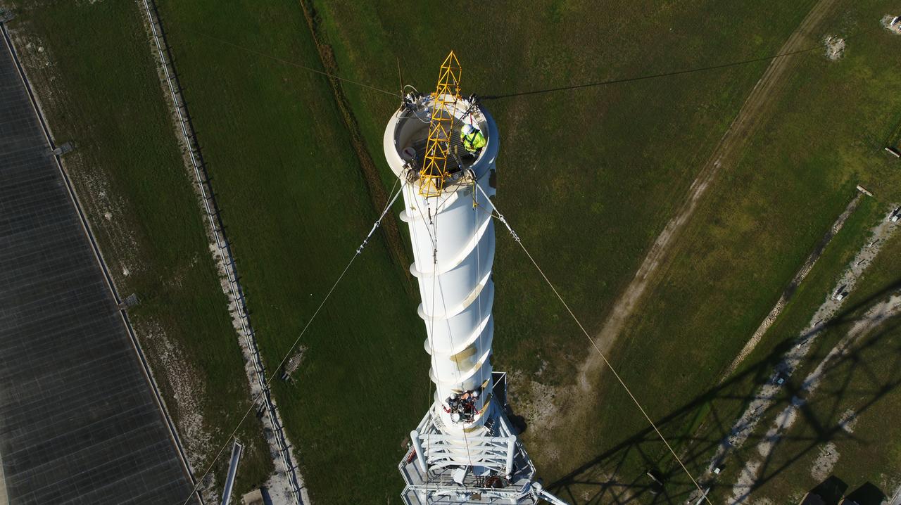 An aerial view shows workers preparing the surface of one of the three lightning protection system towers for painting at Exploration Ground Systems’ Launch Complex 39B at NASA’s Kennedy Space Center in Florida on May 30, 2019. The old paint was removed by the most recent hurricane. Pad 39B is the site of future launches of the agency’s Space Launch System rocket with the Orion spacecraft on Artemis missions. The 600-foot-tall lightning towers will help prevent lightning strikes at the pad during prelaunch and launch activities.