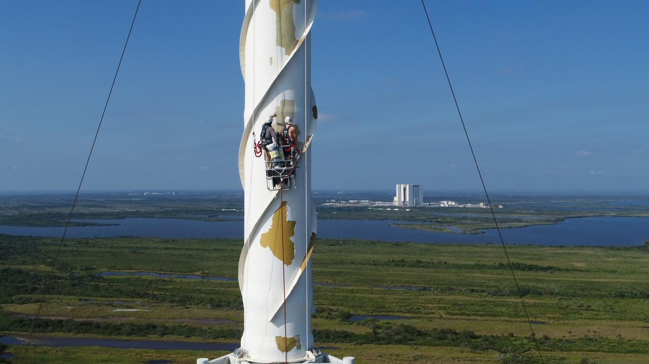 An aerial view shows workers preparing the surface of one of the three lightning protection system towers for painting at Exploration Ground Systems’ Launch Complex 39B at NASA’s Kennedy Space Center in Florida on May 30, 2019. The old paint was removed by the most recent hurricane. Pad 39B is the site of future launches of the agency’s Space Launch System rocket with the Orion spacecraft on Artemis missions. The 600-foot-tall lightning towers will help prevent lightning strikes at the pad during prelaunch and launch activities.