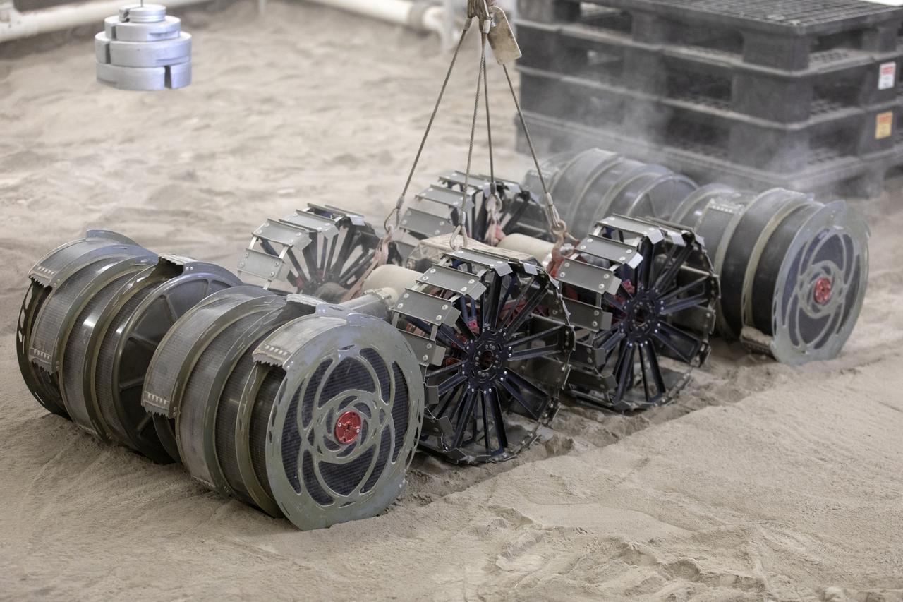 A team from the Granular Mechanics and Regolith Operations Lab tests the Regolith Advanced Surface Systems Operations Robot (RASSOR) in the regolith bin inside Swamp Works at NASA’s Kennedy Space Center in Florida on June 5, 2019. Tests use a gravity assist offload system to simulate reduced gravity conditions found on the Moon. On the surface of the Moon, mining robots like RASSOR will excavate the regolith and take the material to a processing plant where usable elements such as hydrogen, oxygen and water can be extracted for life support systems. RASSOR can scoop up icy regolith which can be used to make operations on the Moon sustainable.