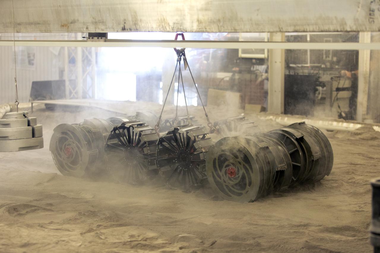 A team from the Granular Mechanics and Regolith Operations Lab tests the Regolith Advanced Surface Systems Operations Robot (RASSOR) in the regolith bin inside Swamp Works at NASA’s Kennedy Space Center in Florida on June 5, 2019. Tests use a gravity assist offload system to simulate reduced gravity conditions found on the Moon. On the surface of the Moon, mining robots like RASSOR will excavate the regolith and take the material to a processing plant where usable elements such as hydrogen, oxygen and water can be extracted for life support systems. RASSOR can scoop up icy regolith which can be used to make operations on the Moon sustainable.