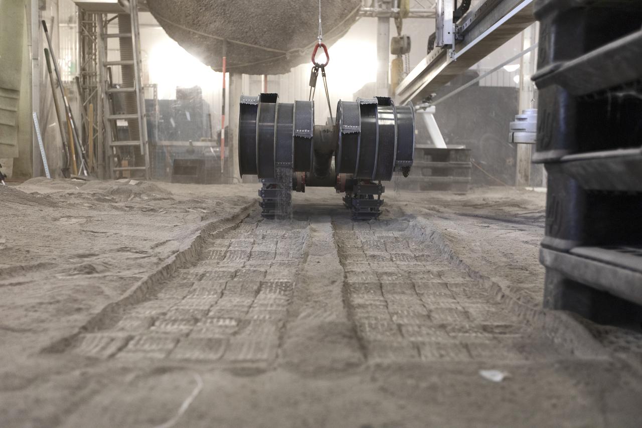 A team from the Granular Mechanics and Regolith Operations Lab tests the Regolith Advanced Surface Systems Operations Robot (RASSOR) in the regolith bin inside Swamp Works at NASA’s Kennedy Space Center in Florida on June 5, 2019. Tests use a gravity assist offload system to simulate reduced gravity conditions found on the Moon. On the surface of the Moon, mining robots like RASSOR will excavate the regolith and take the material to a processing plant where usable elements such as hydrogen, oxygen and water can be extracted for life support systems. RASSOR can scoop up icy regolith which can be used to make operations on the Moon sustainable.