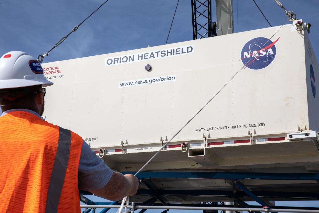 Technicians help secure the shipping container carrying the heat shield for Orion’s Artemis 2 mission, NASA’s first crewed mission, onto a transporter at the agency’s Kennedy Space Center Shuttle Landing Facility in Florida on July 9, 2019. The heat shield, measuring roughly 16 feet in diameter, will protect astronauts upon re-entry on the second mission of Artemis. The heat shield arrived from Lockheed Martin’s manufacturing facility near Denver aboard NASA’s Super Guppy Aircraft. It will be delivered to the Neil Armstrong Operations and Checkout facility high bay. The heat shield is a base titanium truss structure. Over the next several months, technicians will apply Avcoat, an ablative material that will provide the thermal protection. Artemis 2 will confirm all of the spacecraft’s systems operate as designed in the actual environment of deep space with astronauts aboard.
