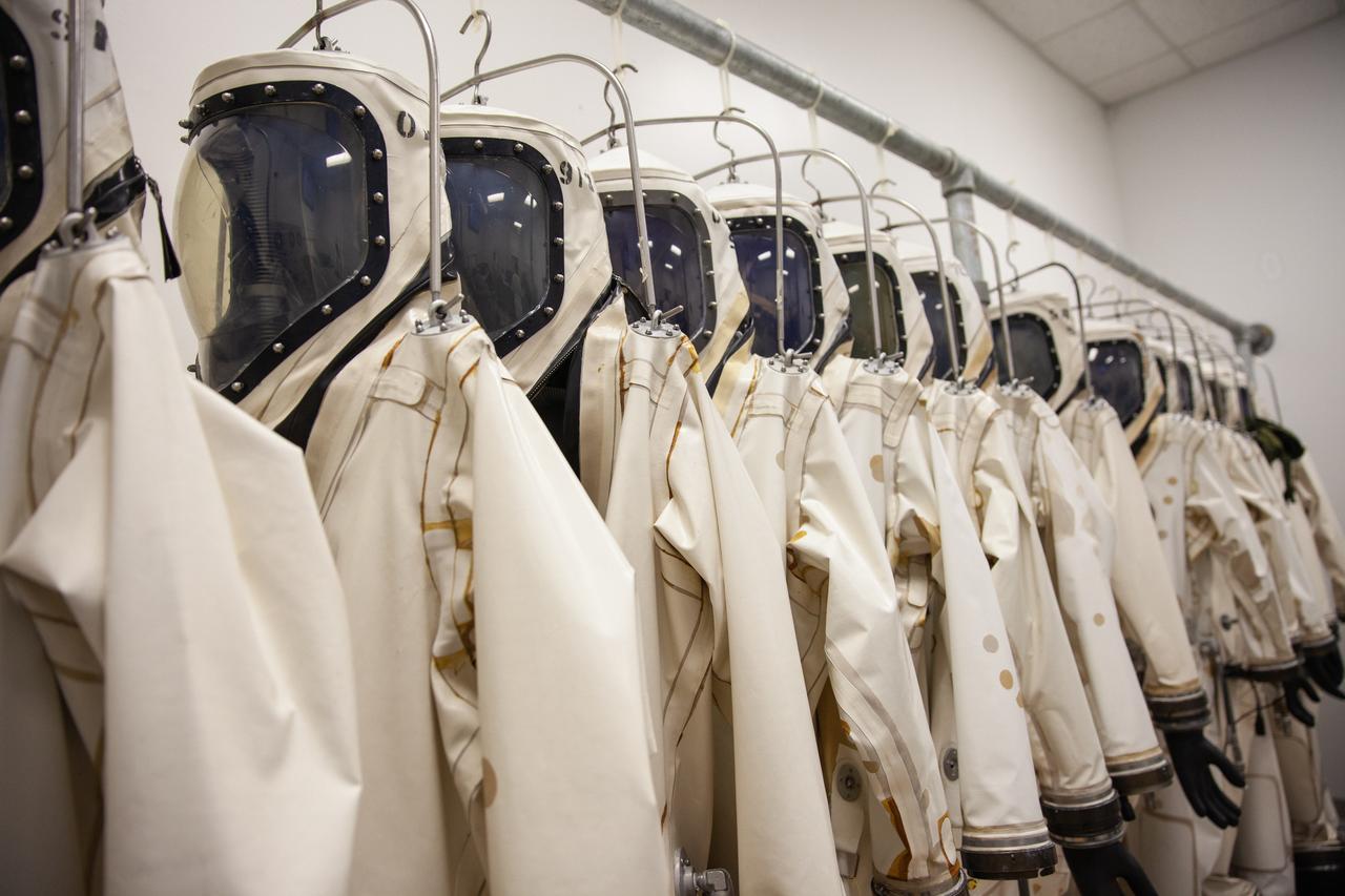 Inside the Multi-Operations Support Building near the Multi-Payload Processing Facility (MPPF) at NASA’s Kennedy Space Center in Florida on Aug. 16, 2019, a row of Self-Contained Atmospheric Protective Ensemble (SCAPE) suits are hanging inside a changing room. SCAPE technicians are practicing putting on the suits for a test simulation of loading propellants into a replicated test tank for Orion. Exploration Ground Systems is preparing for Artemis 1 with a series of hazardous hyper test events at the MPPF. After donning their suits, the technicians will complete a tanking to test the system before Orion arrives for processing. During preparations for launch, these teams will be responsible for loading the Orion vehicle with propellants prior to transportation to the Vehicle Assembly Building, where it will be secured atop the Space Launch System rocket. SCAPE suits are used in operations involving toxic propellants and are supplied with air either through a hardline or through a self-contained environmental control unit.