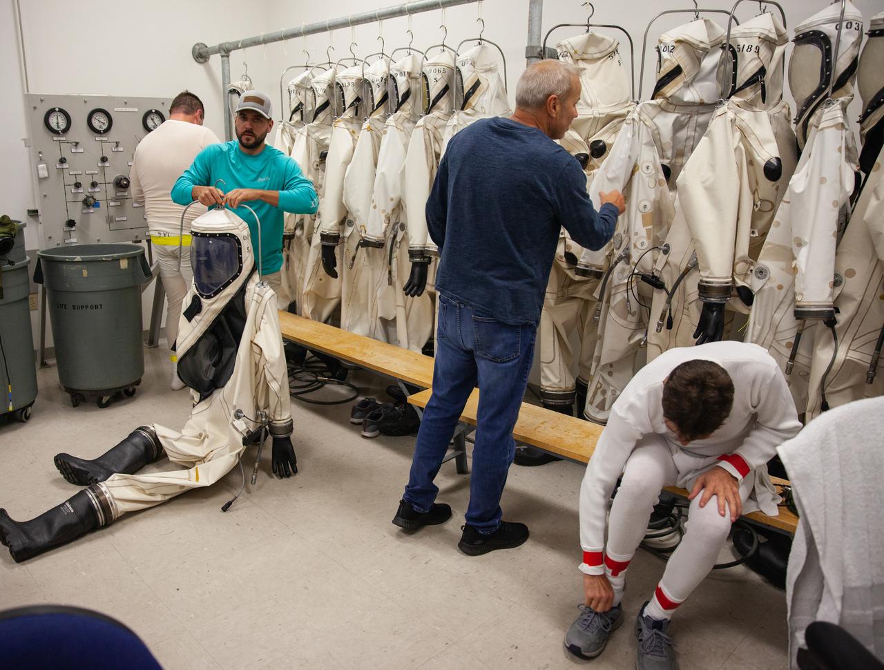 Inside the Multi-Operations Support Building near the Multi-Payload Processing Facility (MPPF) at NASA’s Kennedy Space Center in Florida, technicians are putting on Self-Contained Atmospheric Protective Ensemble (SCAPE) suits inside a changing room on Aug. 16, 2019. SCAPE technicians are practicing by putting on the suits for a test simulation of loading propellants into a replicated test tank for Orion. Exploration Ground Systems is preparing for Artemis 1 with a series of hazardous hyper test events at the MPPF. After donning their suits, the technicians will complete a tanking to test the system before Orion arrives for processing. During preparations for launch, these teams will be responsible for loading the Orion vehicle with propellants prior to transportation to the Vehicle Assembly Building, where it will be secured atop the Space Launch System rocket. SCAPE suits are used in operations involving toxic propellants and are supplied with air either through a hardline or through a self-contained environmental control unit.