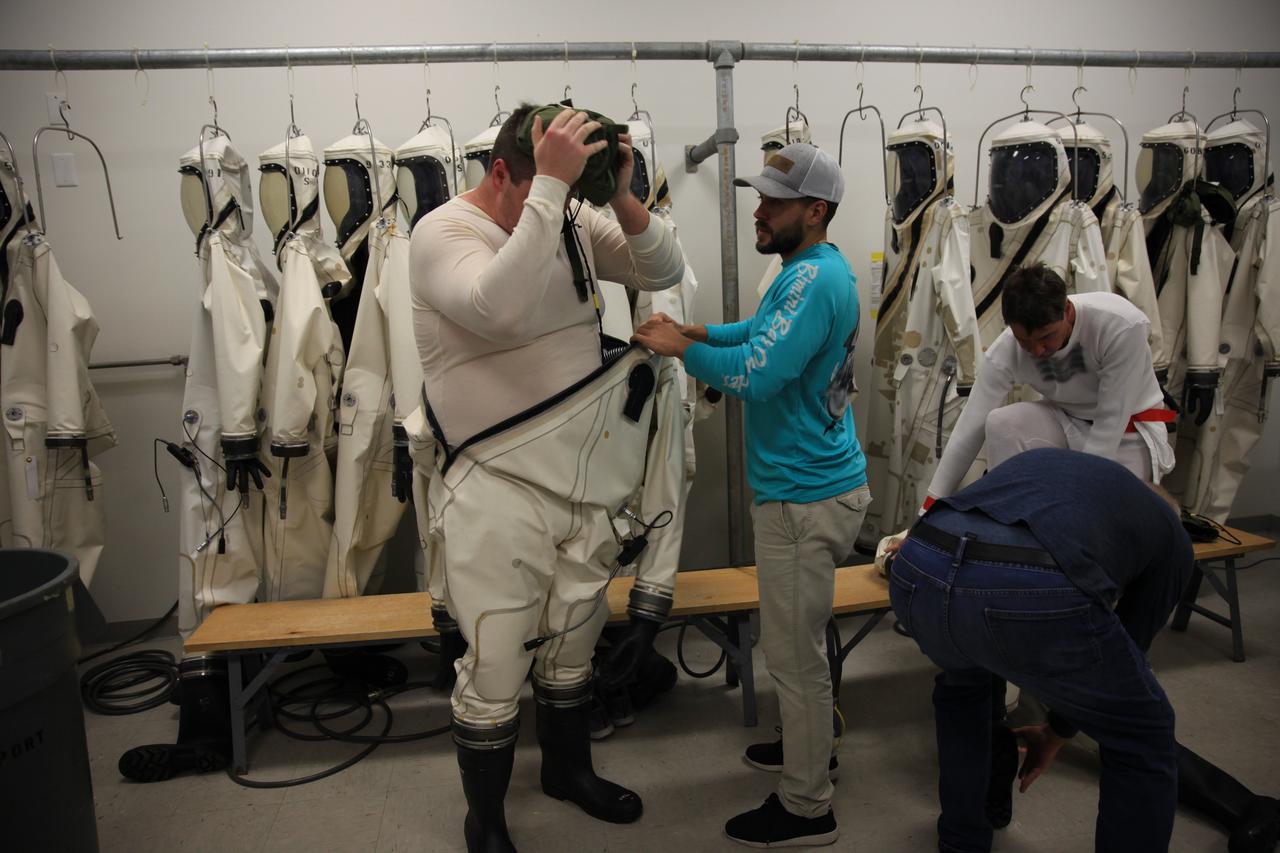 Inside the Multi-Operations Support Building near the Multi-Payload Processing Facility (MPPF) at NASA’s Kennedy Space Center in Florida, technicians put on Self-Contained Atmospheric Protective Ensemble (SCAPE) suits inside a changing room on Aug. 16, 2019. SCAPE technicians are practicing by putting on the suits for a test simulation of loading propellants into a replicated test tank for Orion. Exploration Ground Systems is preparing for Artemis 1 with a series of hazardous hyper test events at the MPPF. After donning their suits, the technicians will complete a tanking to test the system before Orion arrives for processing. During preparations for launch, these teams will be responsible for loading the Orion vehicle with propellants prior to transportation to the Vehicle Assembly Building, where it will be secured atop the Space Launch System rocket. SCAPE suits are used in operations involving toxic propellants and are supplied with air either through a hardline or through a self-contained environmental control unit.