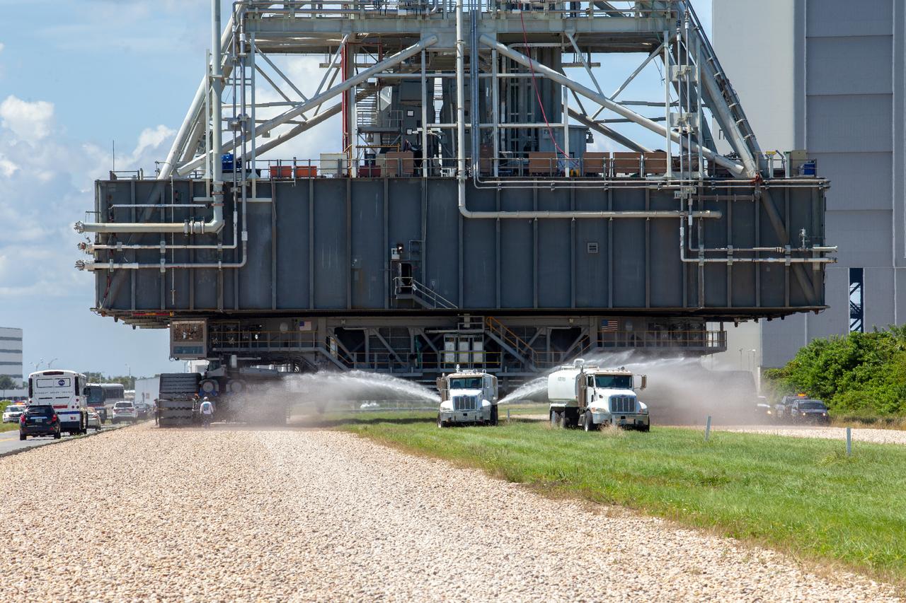NASA’s mobile launcher (ML) atop crawler-transporter 2 moves along the crawlerway on Sept. 10, 2019, after spending a week and a half inside the Vehicle Assembly Building (VAB) at Kennedy Space Center in Florida due to the approach of Hurricane Dorian. Truck in front spray water to reduce dust and sand. The nearly 400-foot-tall structure was moved from Launch Pad 39B to the VAB for safekeeping on Aug. 30. The storm passed about 70 miles east of the spaceport during the overnight hours Tuesday, Sept. 3, and Wednesday, Sept. 4. NASA’s Exploration Ground Systems is moving the mobile launcher back to the launch pad, where teams will complete testing and checkout on the launcher in the coming weeks for the Artemis I mission.