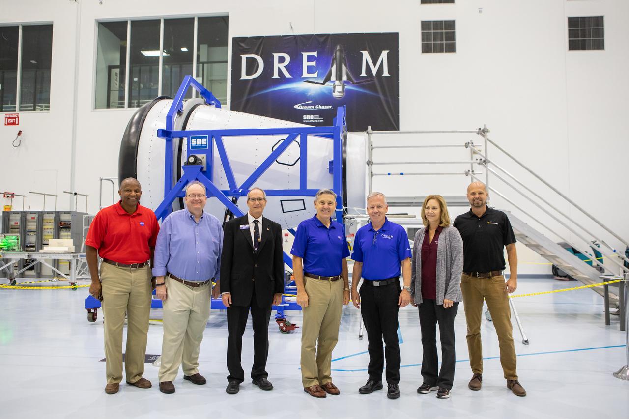 A mockup of the cargo logistics module for Sierra Nevada Corporation’s Dream Chaser, the company’s reusable spaceplane, arrived at the Space Station Processing Facility (SSPF) at NASA’s Kennedy Space Center in Florida in August. On Sept. 20, 2019, senior leadership had the opportunity to view the cargo module in the SSPF high bay. From left are Kelvin Manning, Kennedy associate director, technical; Burt Summerfield, associate director, management; John Roth, vice president, Business Development Space Systems, Sierra Nevada Corporation; Kennedy Center Director Bob Cabana; Steve Lindsey, vice president, Space Exploration Systems, Sierra Nevada Corporation; Kennedy Deputy Director Janet Petro; and Nate Wood, Sierra Nevada Corporation. The SSPF is providing support for current and future NASA and commercial provider programs, including Commercial Resupply Services, Artemis 1, sending the first woman and next man to the Moon, and deep space destinations including Mars.