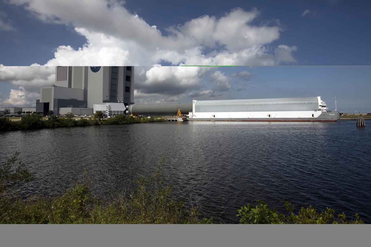 Fluffy clouds serve as a backdrop for the Vehicle Assembly Building (VAB), as the 212-foot-long Space Launch System (SLS) rocket core stage pathfinder is moved inside the Pegasus barge at the Launch Complex 39 turn basin wharf at NASA’s Kennedy Space Center in Florida on Oct. 28, 2019. The core stage pathfinder is a full-scale mock-up of the rocket's core stage. It was used by the Exploration Ground Systems Program and their contractor, Jacobs, to practice offloading, moving and stacking maneuvers inside the VAB, using important ground support equipment to train employees and certify all the equipment works properly. The pathfinder was at Kennedy for about a month. It will make the trek back to NASA's Michoud Assembly Facility in Louisiana.