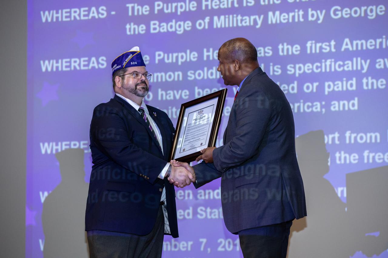 Christopher Vedvick, left, a combat wounded veteran and Military Order of the Purple Heart department of Florida commander, presents Kennedy Space Center’s Associate Director, Technical, Kelvin Manning with a proclamation designating Kennedy a Purple Heart Entity during a Veterans Day observance event on Nov. 7, 2019, in the Training Auditorium. Kennedy is the first NASA center to receive this designation for support and services provided to veterans through the Florida spaceport’s Veterans employee resource group. Attendees included Kennedy employees and more than 20 Purple Heart recipients. Following this recognition, Vedvick, spoke about his experience serving in the United States Army before retiring, his involvement in the Military Order of the Purple Heart and the purpose of the organization. 