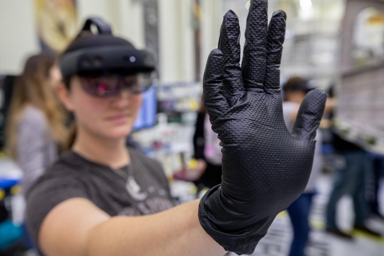 Mary Lakaszcyck, a technician with ASRC Federal Data Solutions, demonstrates a pair of augmented reality (AR) goggles inside the high bay of the Neil Armstrong Operations and Checkout Building at NASA’s Kennedy Space Center in Florida on Jan. 16, 2020. Orion manufacturer Lockheed Martin provided the goggles to technicians to help place tapes where components will be installed on the Orion crew module adapter for NASA’s Artemis II mission, the first crewed mission aboard the spacecraft. Using the AR goggles saves significant labor and time to complete tasks. Manufactured by Microsoft, the goggles, called HoloLens2, are the second version used by Lockheed.