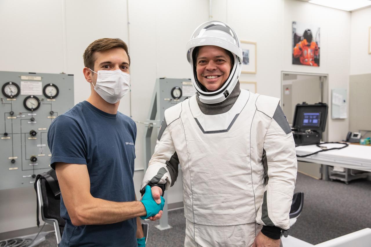 NASA astronauts Bob Behnken, right, wearing a SpaceX spacesuit, and a suit technician shake hands in the Astronaut Crew Quarters at Kennedy Space Center in Florida on Jan. 17, 2020, during a dress rehearsal ahead of the company’s uncrewed In-Flight Abort Test. A SpaceX Falcon 9 rocket and Crew Dragon spacecraft will lift off from Launch Complex 39A on the flight test, which will demonstrate the spacecraft’s escape capabilities in preparation for crewed flights to the International Space Station as part of the agency’s Commercial Crew Program. Behnken and NASA astronaut Doug Hurley are slated to fly on the company’s first crewed mission, Demo-2.