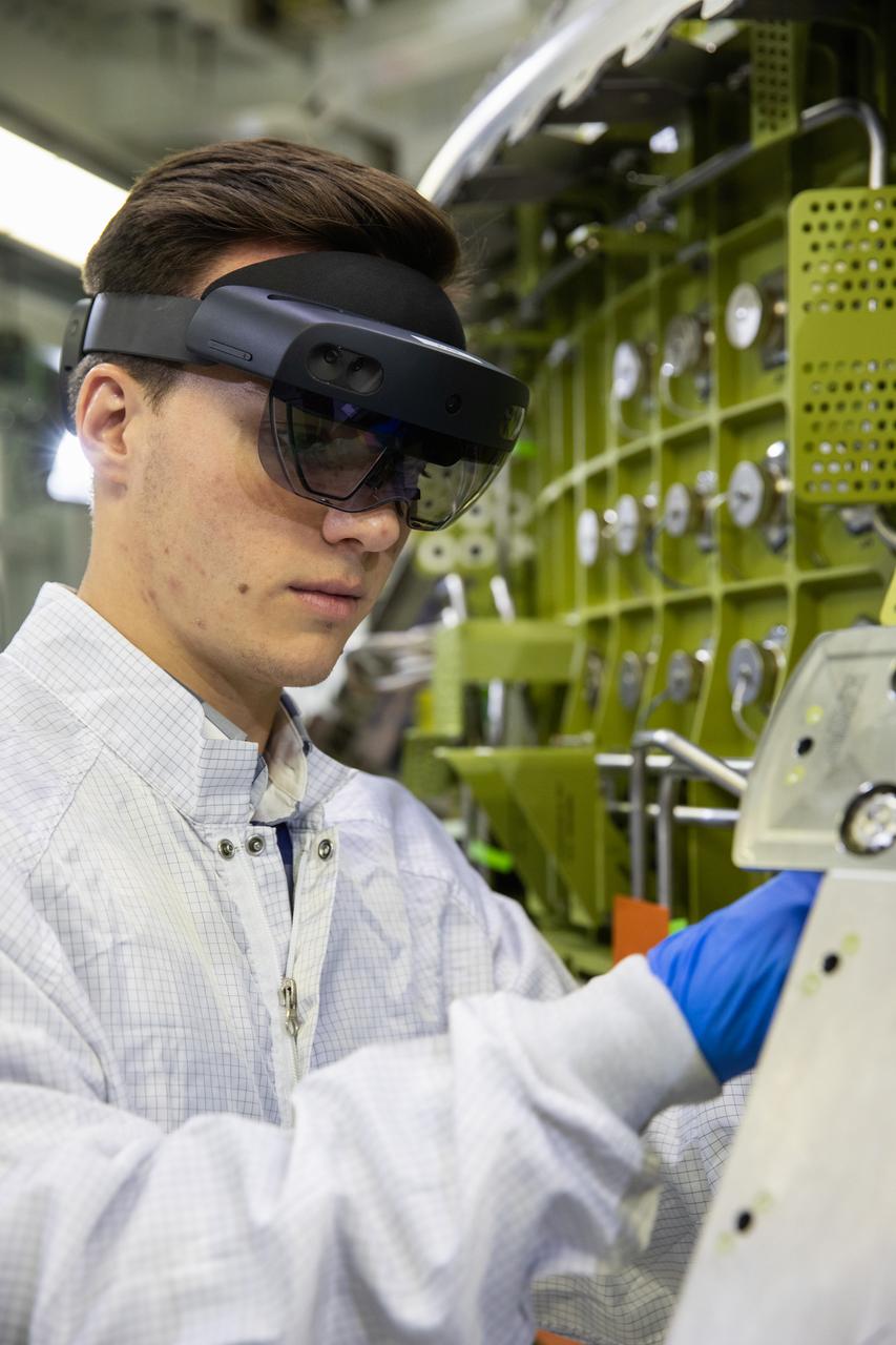 Michael Maxwell, with Lockheed Martin’s augmented reality team, wears a pair of augmented reality (AR) goggles to work on the crew module for NASA’s Artemis II mission inside the high bay of the Neil Armstrong Operations and Checkout Building at the agency’s Kennedy Space Center in Florida on March 18, 2020. Orion manufacturer Lockheed Martin provided the goggles to technicians to help place tapes where components will be installed on the crew module adapter for Artemis II, the first crewed mission aboard the spacecraft. Using the AR goggles saves significant labor and time to complete tasks. Manufactured by Microsoft, the goggles, called HoloLens2, are the second version used by Lockheed.