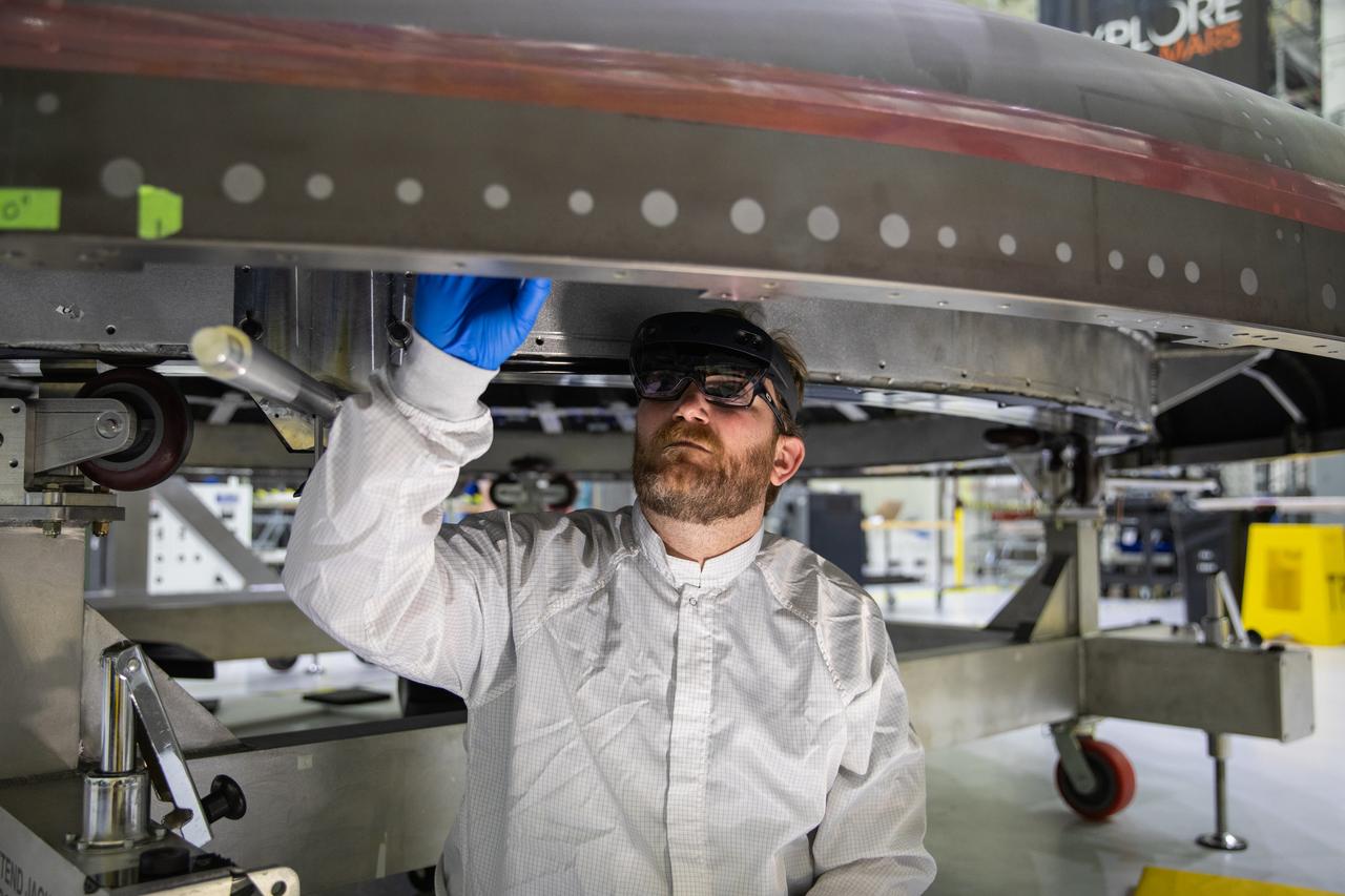 Eric Nolan, a technician with ASRC Federal Data Solutions, wears a pair of augmented reality (AR) goggles as he works on the heat shield for the crew module for NASA’s Artemis II mission inside the high bay of the Neil Armstrong Operations and Checkout Building at the agency’s Kennedy Space Center in Florida on March 18, 2020. Orion manufacturer Lockheed Martin provided the goggles to technicians to help place tapes where components will be installed on Orion for Artemis II, the first crewed mission aboard the spacecraft. Using the AR goggles saves significant labor and time to complete tasks. Manufactured by Microsoft, the goggles, called HoloLens2, are the second version used by Lockheed.