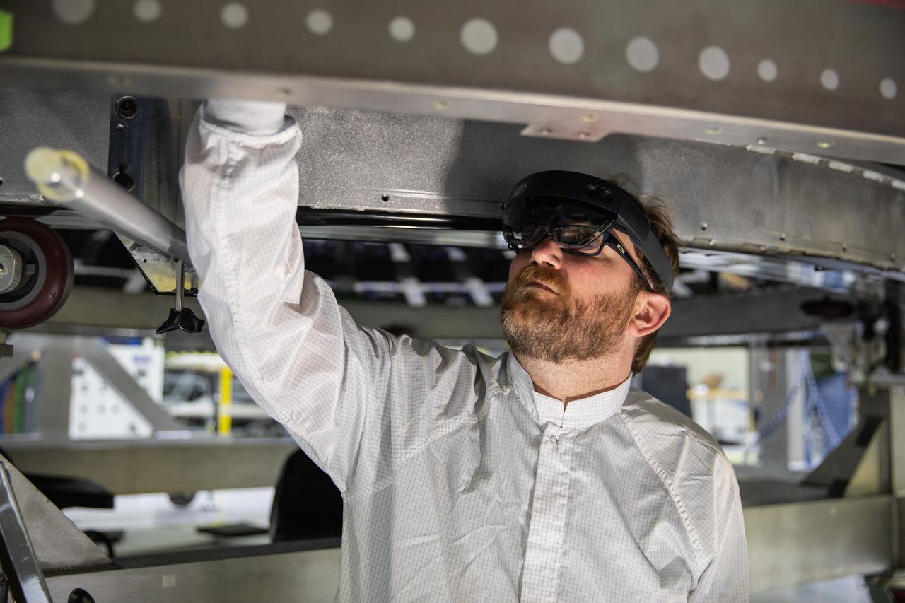 Eric Nolan, a technician with ASRC Federal Data Solutions, wears a pair of augmented reality (AR) goggles as he works on the heat shield for the crew module for NASA’s Artemis II mission inside the high bay of the Neil Armstrong Operations and Checkout Building at the agency’s Kennedy Space Center in Florida on March 18, 2020. Orion manufacturer Lockheed Martin provided the goggles to technicians to help place tapes where components will be installed on Orion for Artemis II, the first crewed mission aboard the spacecraft. Using the AR goggles saves significant labor and time to complete tasks. Manufactured by Microsoft, the goggles, called HoloLens2, are the second version used by Lockheed.