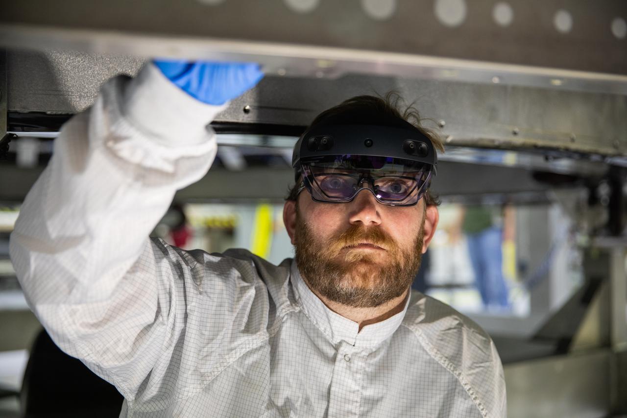 Eric Nolan, a technician with ASRC Federal Data Solutions, wears a pair of augmented reality (AR) goggles as he works on the heat shield for the crew module for NASA’s Artemis II mission inside the high bay of the Neil Armstrong Operations and Checkout Building at the agency’s Kennedy Space Center in Florida on March 18, 2020. Orion manufacturer Lockheed Martin provided the goggles to technicians to help place tapes where components will be installed on Orion for Artemis II, the first crewed mission aboard the spacecraft. Using the AR goggles saves significant labor and time to complete tasks. Manufactured by Microsoft, the goggles, called HoloLens2, are the second version used by Lockheed.