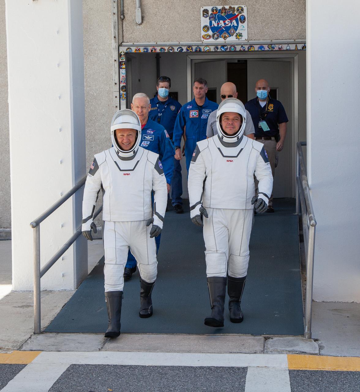 On May 23, 2020, Demo-2 crew members Robert Behnken (right) and Douglas Hurley walk out of the Neil A. Armstrong Operations and Checkout Building at NASA’s Kennedy Space Center in Florida in preparation for transport to Launch Complex 39A during a full dress rehearsal ahead of launch. A SpaceX Falcon 9 rocket and Crew Dragon spacecraft will carry Behnken and Hurley to the International Space Station as part of the agency’s Commercial Crew Program, returning human spaceflight capability to the U.S. after nearly a decade. Launch is slated for 4:33 p.m. EDT on Wednesday, May 27.