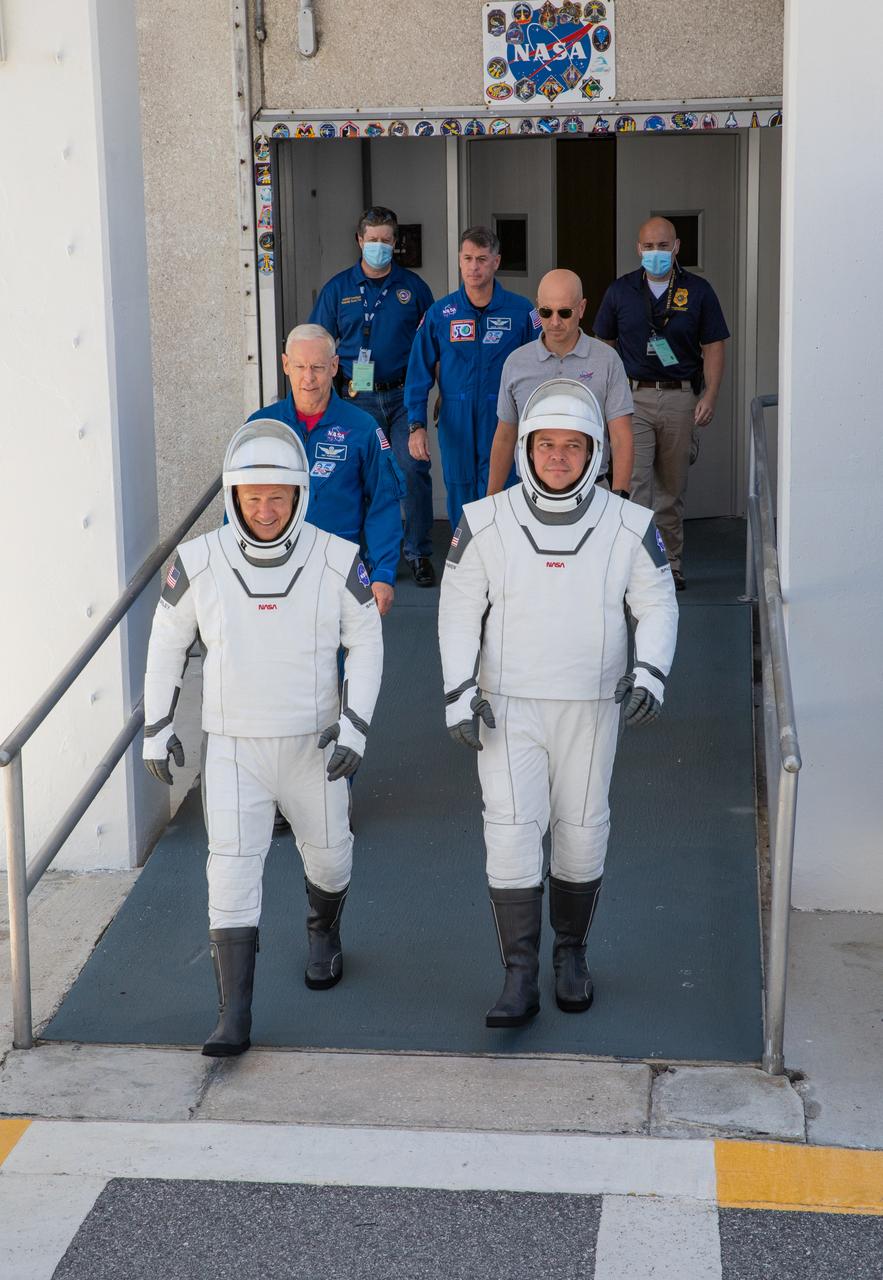 On May 23, 2020, Demo-2 crew members Robert Behnken (right) and Douglas Hurley walk out of the Neil A. Armstrong Operations and Checkout Building at NASA’s Kennedy Space Center in Florida in preparation for transport to Launch Complex 39A during a full dress rehearsal ahead of launch. A SpaceX Falcon 9 rocket and Crew Dragon spacecraft will carry Behnken and Hurley to the International Space Station as part of the agency’s Commercial Crew Program, returning human spaceflight capability to the U.S. after nearly a decade. Launch is slated for 4:33 p.m. EDT on Wednesday, May 27.