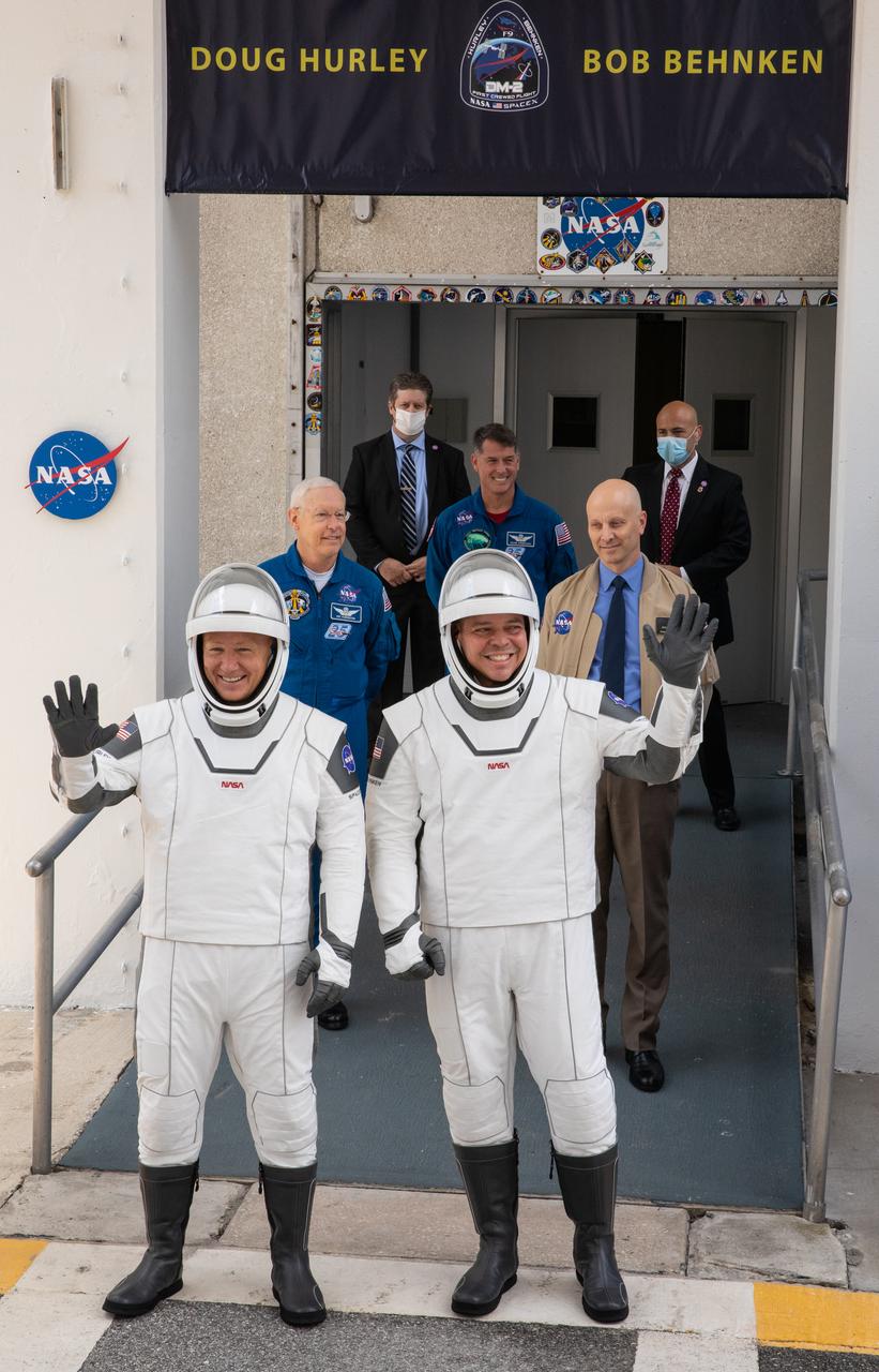 NASA astronauts Douglas Hurley (left) and Robert Behnken wave as they exit the Neil A. Armstrong Operations and Checkout Building at the agency’s Kennedy Space Center in Florida in preparation for transport to Launch Complex 39A to launch on NASA’s SpaceX Demo-2 mission. The launch, initially scheduled for May 27, 2020, was scrubbed due to unfavorable weather conditions around Launch Complex 39A. The next launch attempt will be Saturday, May 30. Liftoff of the SpaceX Falcon 9 rocket and Crew Dragon spacecraft is scheduled for 3:22 p.m. EDT from historic Launch Complex 39A. Behnken and Hurley will be the first astronauts to launch to the International Space Station from U.S. soil since the end of the Space Shuttle Program in 2011. Part of NASA’s Commercial Crew Program, this will be SpaceX’s final flight test, paving the way for the agency to certify the crew transportation system for regular, crewed flights to the orbiting laboratory.