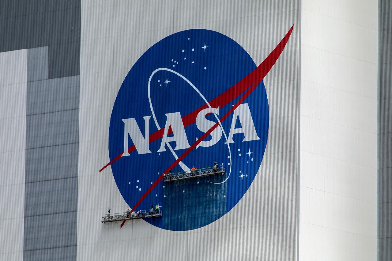 Painting of the NASA logo, also called the meatball, continues on the 525-foot-tall Vehicle Assembly Building (VAB) at the agency’s Kennedy Space Center in Florida on May 29 2020. HM2 and H.I.S. Painting of Titusville, Florida, are repainting the meatball and the American Flag on the iconic building. High Bay 3 inside the VAB has been upgraded with 10 new levels of work platforms that will surround and provide access for service and processing of NASA's Space Launch System (SLS) rocket and Orion spacecraft. Exploration Ground Systems is overseeing upgrades to the VAB to support the launch of the SLS and Orion for Artemis missions. Under the Artemis program, NASA will send the first woman and next man to the Moon.