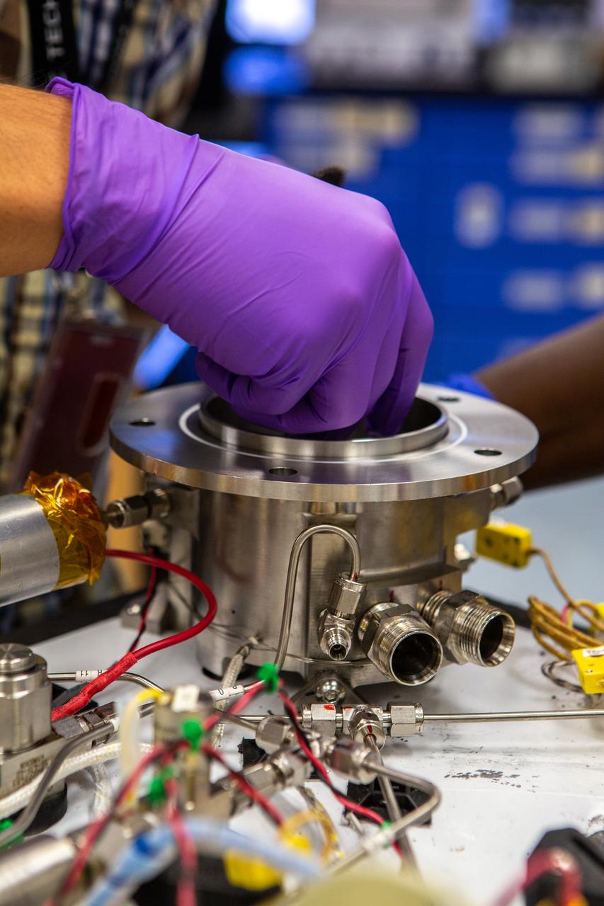 Technicians wearing protective equipment perform work for a future mission on flight hardware for NASA’s Orbital Syngas Commodity Augmentation Reactor, or OSCAR, at the Neil Armstrong Operations and Checkout Facility at the agency’s Kennedy Space Center in Florida on Aug. 10, 2020. OSCAR began as an Early Career Initiative project at the spaceport that studies technology to convert trash and human waste into useful gasses such as methane, hydrogen, and carbon dioxide. By processing small pieces of trash in a high-temperature reactor, OSCAR is advancing new and innovative technology for managing waste in space.