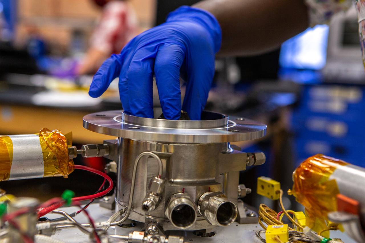 Technicians wearing protective equipment perform work for a future mission on flight hardware for NASA’s Orbital Syngas Commodity Augmentation Reactor, or OSCAR, at the Neil Armstrong Operations and Checkout Facility at the agency’s Kennedy Space Center in Florida on Aug. 10, 2020. OSCAR began as an Early Career Initiative project at the spaceport that studies technology to convert trash and human waste into useful gasses such as methane, hydrogen, and carbon dioxide. By processing small pieces of trash in a high-temperature reactor, OSCAR is advancing new and innovative technology for managing waste in space.
