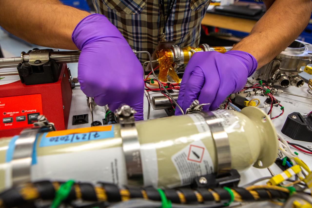 Technicians wearing protective equipment perform work for a future mission on flight hardware for NASA’s Orbital Syngas Commodity Augmentation Reactor, or OSCAR, at the Neil Armstrong Operations and Checkout Facility at the agency’s Kennedy Space Center in Florida on Aug. 10, 2020. OSCAR began as an Early Career Initiative project at the spaceport that studies technology to convert trash and human waste into useful gasses such as methane, hydrogen, and carbon dioxide. By processing small pieces of trash in a high-temperature reactor, OSCAR is advancing new and innovative technology for managing waste in space.