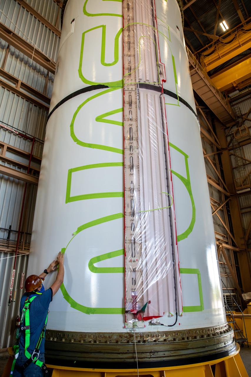Workers with NASA’s Exploration Ground Systems (EGS) use a laser projector and green tape to mask off the shape of the agency’s “worm” logo on the side of an Artemis I solid rocket booster segment inside the Rotation, Processing and Surge Facility (RPSF) at Kennedy Space Center in Florida, Sept. 3, 2020. The booster segments will help propel the Space Launch System (SLS) rocket on Artemis I, a test of the Orion spacecraft and SLS as an integrated system ahead of crewed flights to the Moon. Northrop Grumman, which built the booster segments, is covering the cost of the painting.
