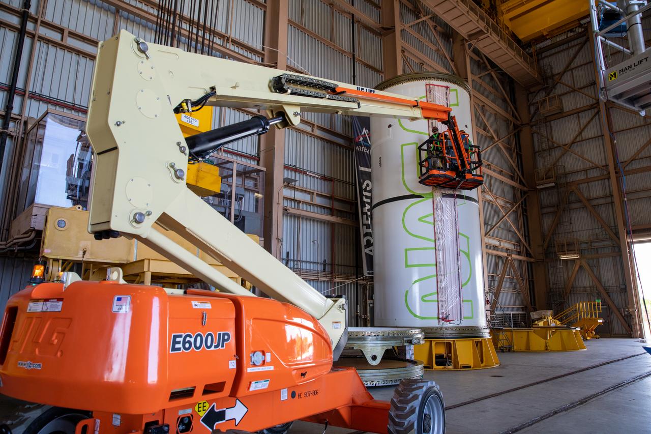 Workers with NASA’s Exploration Ground Systems (EGS) use a laser projector and green tape to mask off the shape of the agency’s “worm” logo on the side of an Artemis I solid rocket booster segment inside the Rotation, Processing and Surge Facility (RPSF) at Kennedy Space Center in Florida, Sept. 3, 2020. The booster segments will help propel the Space Launch System (SLS) rocket on Artemis I, a test of the Orion spacecraft and SLS as an integrated system ahead of crewed flights to the Moon. Northrop Grumman, which built the booster segments, is covering the cost of the painting.