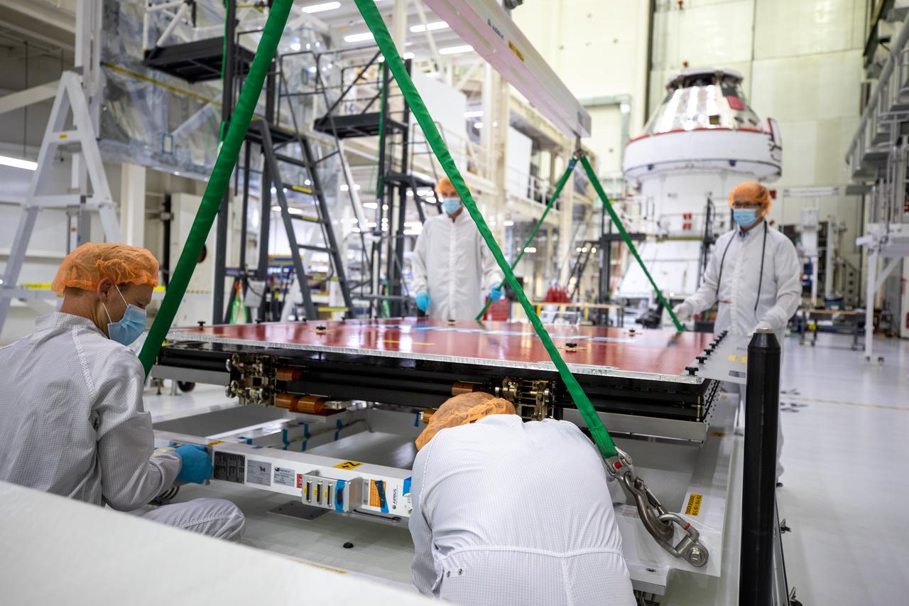Technicians with European Service Module processing teams from the European Space Agency, Airbus, and Airbus Netherlands assist with securing a protective cover as a crane prepares to lift the panel during installation of one of four solar array wings inside the Neil Armstrong Operations and Checkout Building high bay at NASA’s Kennedy Space Center in Florida on Sept. 23, 2020. The Orion spacecraft for Artemis I is shown in the background. The solar arrays were extended, inspected, and then retracted, before installation on the spacecraft. Each solar array panel will generate 11 kilowatts of power and span about 63 feet. The array is a component of Orion’s service module, which is provided by the European Space Agency and built by Airbus Defence and Space to supply Orion’s power, propulsion, air and water. The first in a series of increasingly complex missions, Artemis I will test the Orion spacecraft and Space Launch System as an integrated system ahead of crewed flights to the Moon. Under the Artemis program, NASA will land the first woman and the next man on the Moon in 2024.