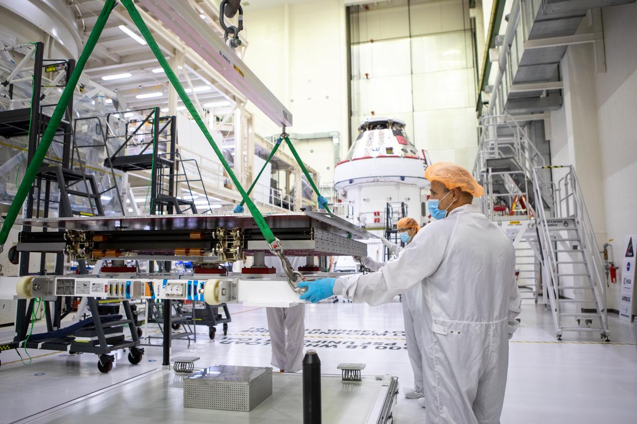 Technicians with European Service Module processing teams from the European Space Agency, Airbus, and Airbus Netherlands assist with securing a protective cover as a crane prepares to lift the panel during installation of one of four solar array wings inside the Neil Armstrong Operations and Checkout Building high bay at NASA’s Kennedy Space Center in Florida on Sept. 23, 2020. The Orion spacecraft for Artemis I is shown in the background. The solar arrays were extended, inspected, and then retracted, before installation on the spacecraft. Each solar array panel will generate 11 kilowatts of power and span about 63 feet. The array is a component of Orion’s service module, which is provided by the European Space Agency and built by Airbus Defence and Space to supply Orion’s power, propulsion, air and water. The first in a series of increasingly complex missions, Artemis I will test the Orion spacecraft and Space Launch System as an integrated system ahead of crewed flights to the Moon. Under the Artemis program, NASA will land the first woman and the next man on the Moon in 2024.
