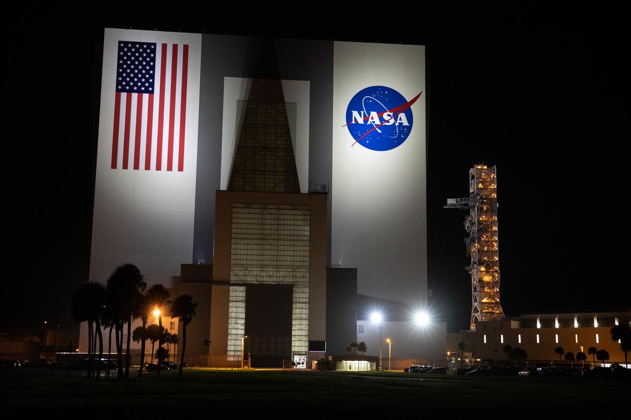 Bright lights illuminate the Vehicle Assembly Building in the early morning on Oct. 20, 2020, as the mobile launcher for the Artemis I mission begins its rollout atop crawler-transporter 2 at NASA’s Kennedy Space Center in Florida. The nearly 400-foot-tall mobile launcher is being rolled to Launch Pad 39B. During its two-week stay at the pad, engineers with Exploration Ground Systems and Jacobs will perform several tasks, including a timing test to validate the launch team’s countdown timeline, and a thorough, top-to-bottom wash down of the mobile launcher to remove any debris remaining from construction and installation of the umbilical arms. Artemis I will test the Orion spacecraft and Space Launch System as an integrated system ahead of crewed flights to the Moon. Under the Artemis program, NASA will land the first woman and the next man on the Moon in 2024.