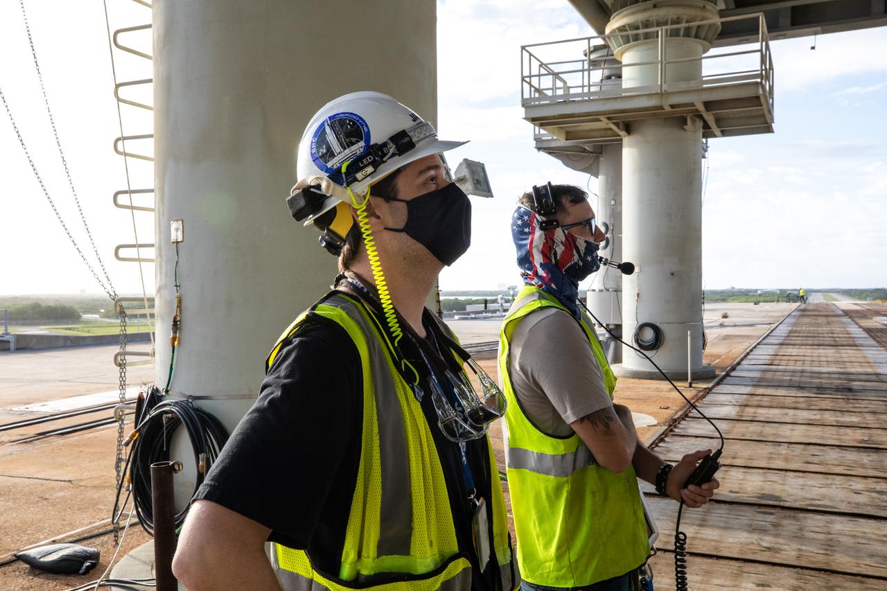 Workers stand on the surface of Launch Pad 39B at NASA’s Kennedy Space Center in Florida on Oct. 23, 2020. They are monitoring launch countdown timeline demonstration activities occurring on the mobile launcher for Artemis I. The nearly 400-foot-tall mobile launcher is at the pad while engineers with Exploration Ground Systems and Jacobs complete several tasks, including a timing test to validate the launch team’s countdown timeline, and a thorough, top-to-bottom wash down of the mobile launcher to remove any debris remaining from construction and installation of the umbilical arms. Artemis I will test the Orion spacecraft and Space Launch System as an integrated system ahead of crewed flights to the Moon. Under the Artemis program, NASA will land the first woman and the next man on the Moon in 2024.