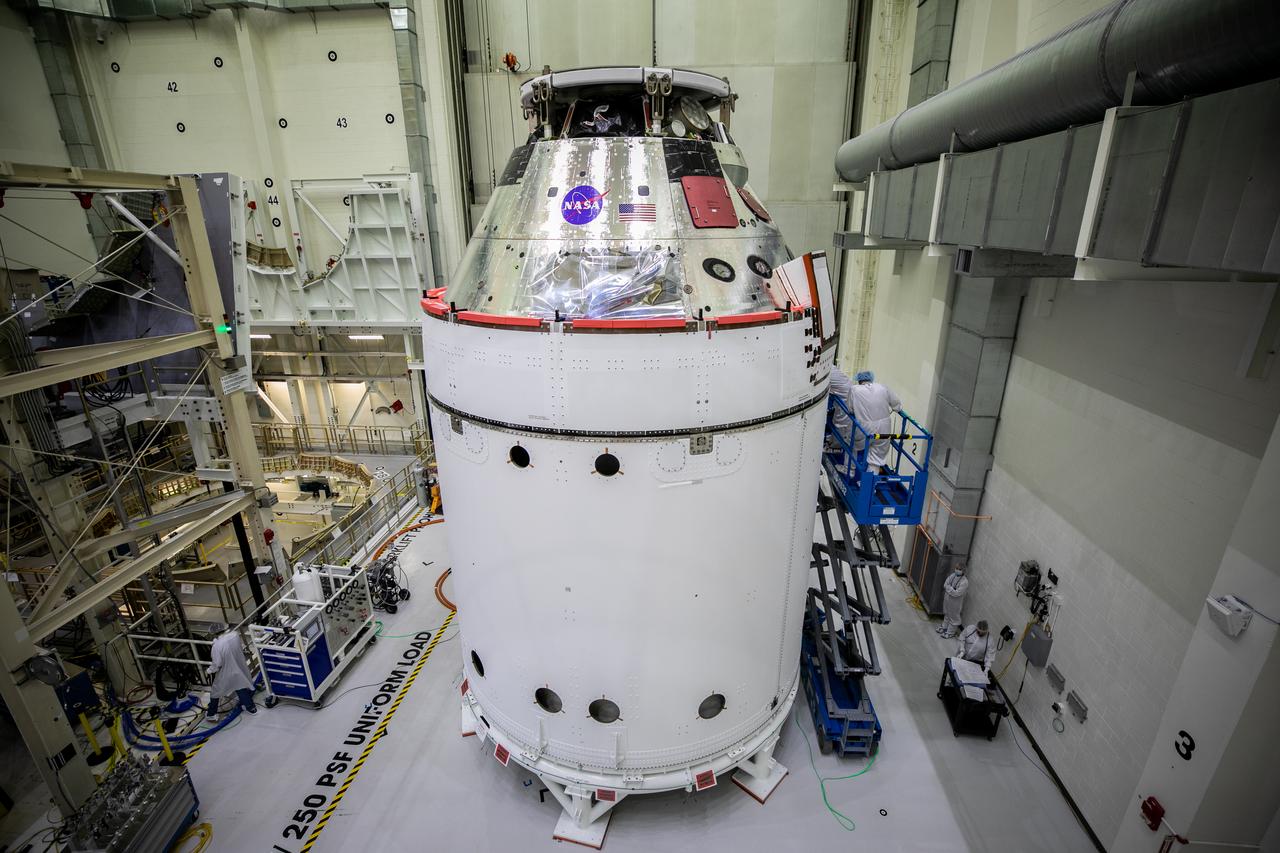 The Orion spacecraft for NASA’s Artemis I mission is in view inside the Neil Armstrong Operations and Checkout Building high bay on Oct. 28, 2020, at NASA’s Kennedy Space Center in Florida. The NASA insignia, also called the “meatball,” and the American Flag have been applied to the Orion crew module back shell. Attached below Orion are the crew module adapter and the European Service Module (ESM) with spacecraft adapter jettison fairings installed. Recently, teams from across the globe installed the four solar array wings, which are housed inside the protective covering of the fairings. The fairing panels will encapsulate the ESM to protect it from harsh environments such as heat, wind, and acoustics as the spacecraft is propelled out of Earth’s atmosphere atop the Space Launch System rocket during NASA’s Artemis I mission.